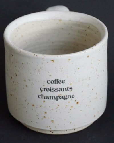 Tasse aus Ton mit Spots gedreht und mit Sahne matt glasiert, Aufschrift coffee, croissants, champagne untereinander stehend