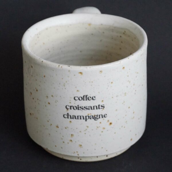 Tasse aus Ton mit Spots gedreht und mit Sahne matt glasiert, Aufschrift coffee, croissants, champagne untereinander stehend